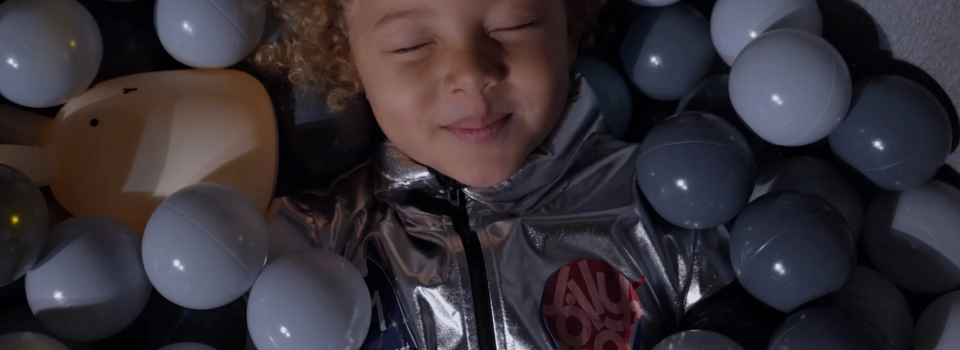 Young boy in sea of balls, smiling and closing his eyes.